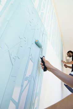 two people are painting a wall with blue paint