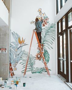 a woman is painting a mural on the side of a building while she stands on a ladder