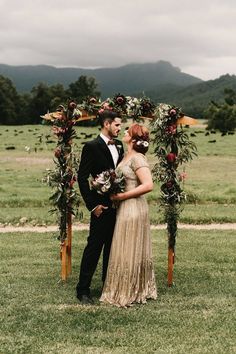 a bride and groom standing under an arch decorated with greenery in the middle of a field