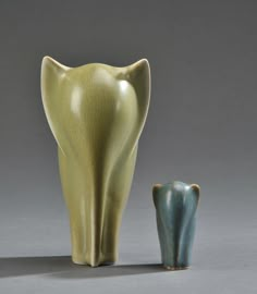 two vases sitting next to each other on a gray surface, one with an open mouth