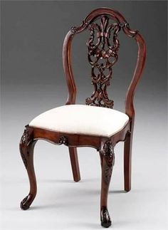 an ornate wooden chair with a white cushion on the seat and backrest, against a gray background