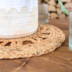 a glass vase sitting on top of a wooden table next to a straw mat with a flower in it