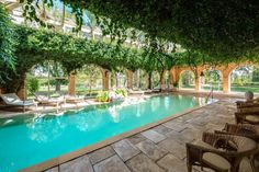 an indoor swimming pool surrounded by greenery and stone patio furniture with wicker chairs