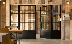 the interior of a restaurant with wooden walls and black glass doors that lead to an outside dining area