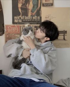 a woman holding a cat in her arms while sitting on a bed with posters behind her