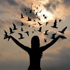 a woman with birds flying above her head in the sky at sunset or dawn, silhouetted by clouds