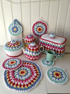 a crocheted table set with tea pot, plates and cups on it next to a white wall