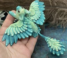 a hand holding a green and blue bird figurine with feathers in the background