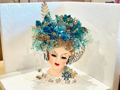 a mannequin head is adorned with blue flowers and leaves, while wearing a tiara