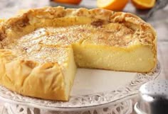 a pie sitting on top of a white plate next to an oranges in the background