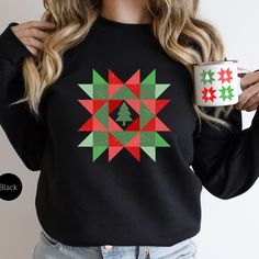 a woman is holding a coffee mug and wearing a black sweater with christmas decorations on it