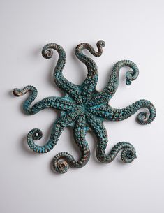 an octopus made out of turquoise beads on a white surface with spirals in the middle