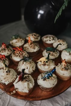 cupcakes with white frosting and dinosaur figurines on a wooden plate