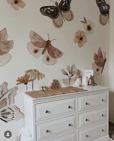 a white dresser topped with lots of drawers next to a wall covered in butterfly decals