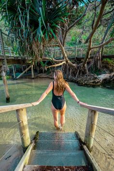 a woman in a black swimsuit standing on a wooden bridge