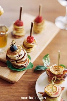 there are many small sandwiches on the table with fruit and syrups in glasses next to them