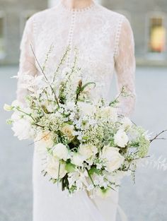 a woman holding a bouquet of flowers in her hand and wearing a white dress with sheer sleeves