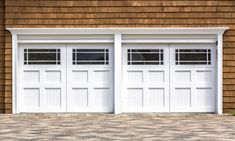 two white garage doors on the side of a brown building with brick flooring and windows