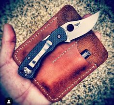 a hand holding a small knife in a brown leather case on top of a carpeted floor