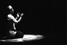 a man sitting on the ground in the dark with his hands clasped to his chest