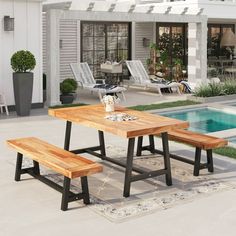 a wooden table and bench in front of a swimming pool with lounge chairs around it