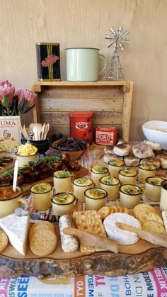 an assortment of food is displayed on a table with flowers and other items in the background