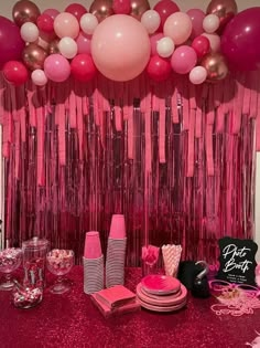 a table topped with lots of pink and white balloons next to a wall covered in streamers