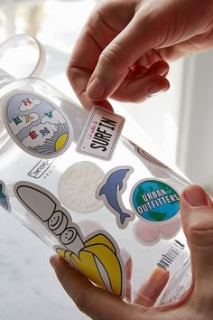 someone holding onto a clear water bottle with stickers on the lid and around it