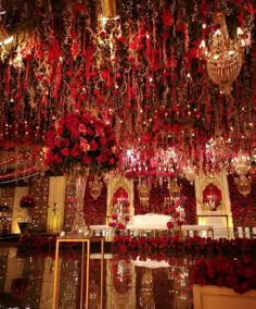 a room filled with lots of red flowers and chandeliers hanging from the ceiling