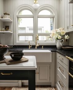 a white kitchen with black counter tops and gold trim on the windowsills, along with a bowl of flowers