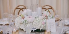 a centerpiece with white flowers and candles is displayed on a table set for a formal dinner