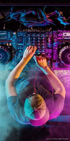 a dj mixing in front of some colorful lights and sound equipment with his hands up