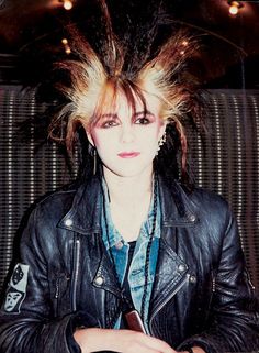 a woman sitting in a chair with her hair up and wearing a black leather jacket