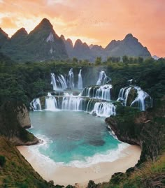 the waterfall is surrounded by green trees and blue water as the sun sets in the background