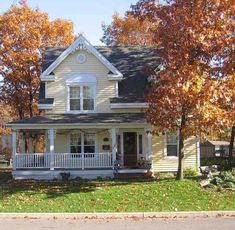 a white house sitting on the side of a road in front of trees with orange leaves