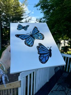 a person holding up a piece of paper with blue butterflies on it