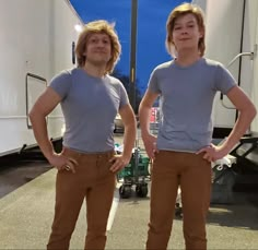 two men standing next to each other in front of a white trailer with their hands on their hipss