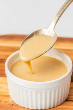 a spoon full of gravy sitting in a white bowl on top of a wooden cutting board