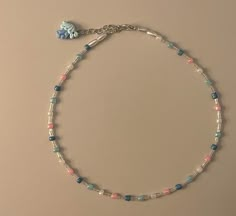 a bracelet with blue, pink and white beads is displayed on a beige table top