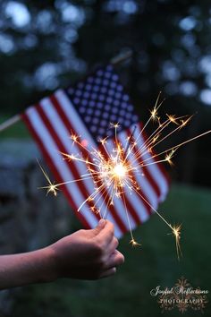 someone holding a sparkler in front of an american flag