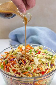 someone pouring dressing into a salad in a glass bowl