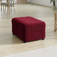 a red ottoman sitting on top of a hard wood floor next to a potted plant