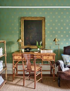 an old fashioned desk and chair in a room with green wallpaper, gold framed painting on the wall