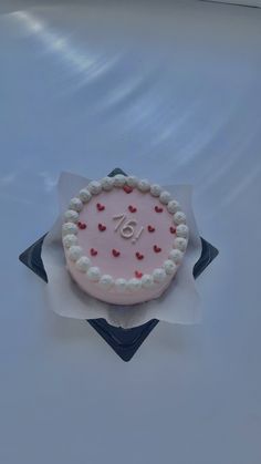 a pink cake with white frosting and red hearts on it sitting on top of a table