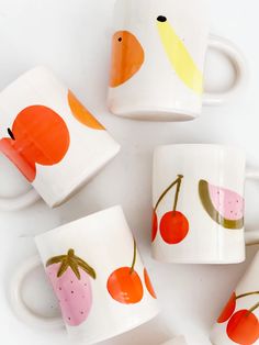 four coffee mugs with fruit painted on them sitting next to each other in front of a white background