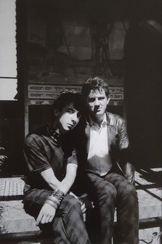 black and white photograph of two people sitting on steps outside an old building, one man has his arm around the woman's shoulder