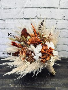 an arrangement of dried flowers and feathers on a wooden table in front of a brick wall