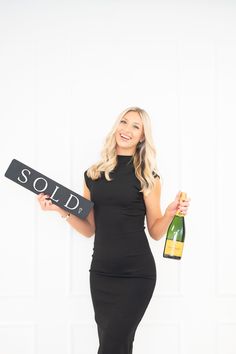 a woman in a black dress holding a wine bottle and a sign that says sold