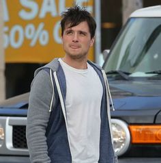 a young man is standing in front of a car and has his hands in his pockets