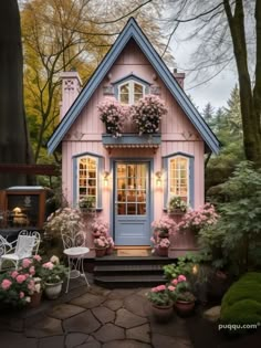 a pink and blue house with flowers on the front door, sitting next to some trees